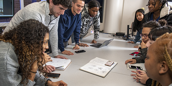 Nine students around a table working together.