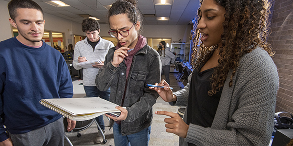 Three students talking and reviewing a notebook.