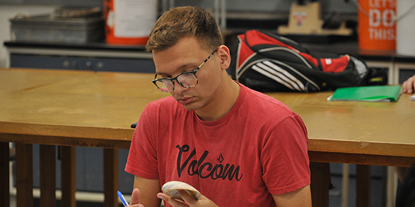 A student in a classroom looking down at an object in their hands.