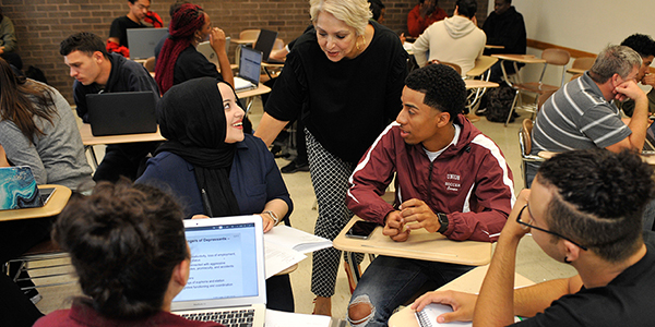 A professor talking with a group of students in a classroom.