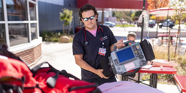 A paramedic student holding a portable medical device in a training setting.