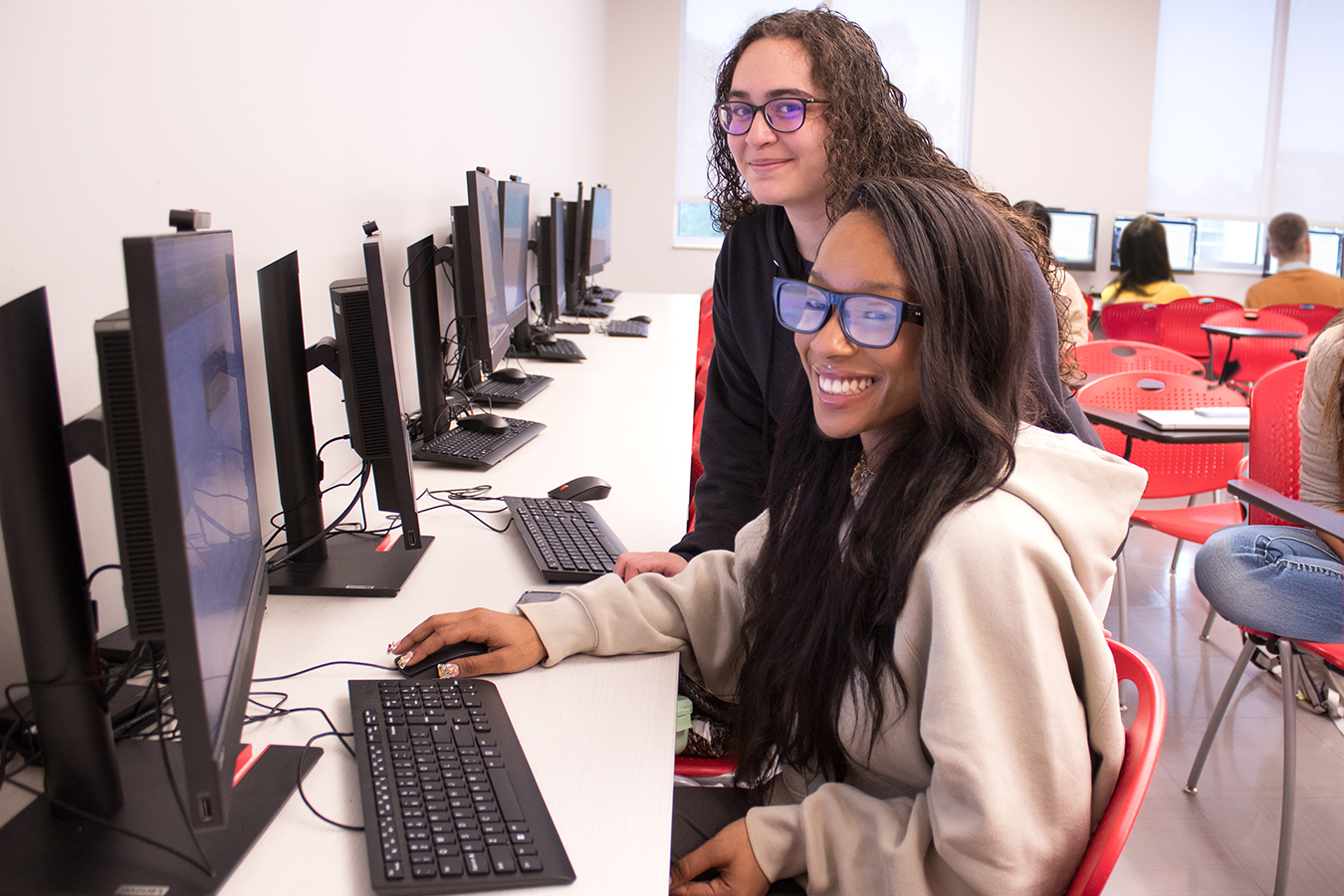 Two people smiling while wokring on a computer.