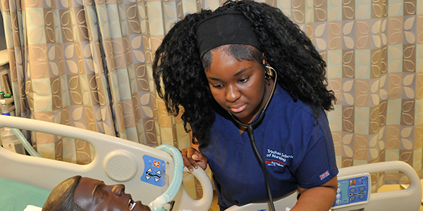A student using a stethoscope on a medical training mannequin.