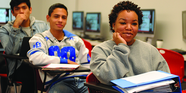 Three students sitting in desks in a classroom.