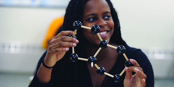 A student smiling while holding an object in a classroom.