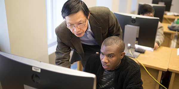 A professor helping a student using the computer.