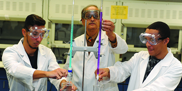 A professor working with two students in a chemistry lab.