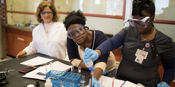 A professor observing two students as they conduct an experiment in a laboratory.