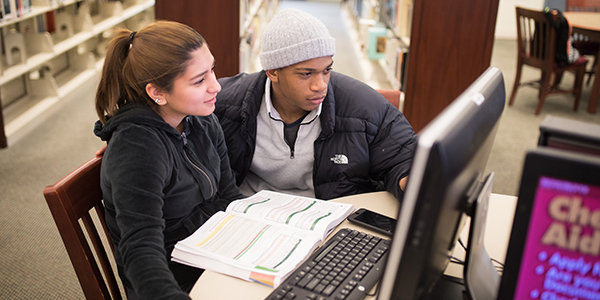 Two students sitting looking at a desktop computer.