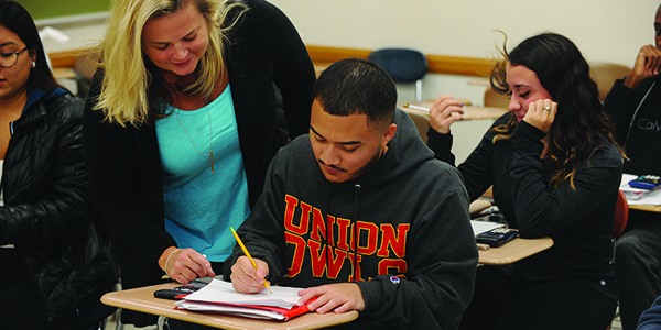 A professor helping a student with an assignment in a classroom.