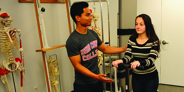A student using a physical therapy device while another student provides assistance.
