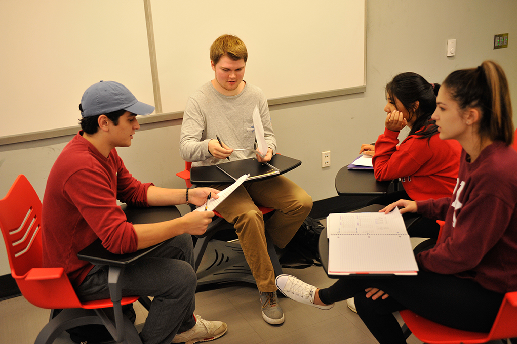 A group of four students sitting and talking in a classroom.